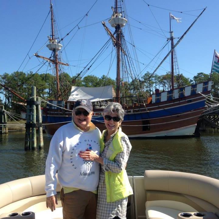 a couple standing in a pontoon boat on a body of water