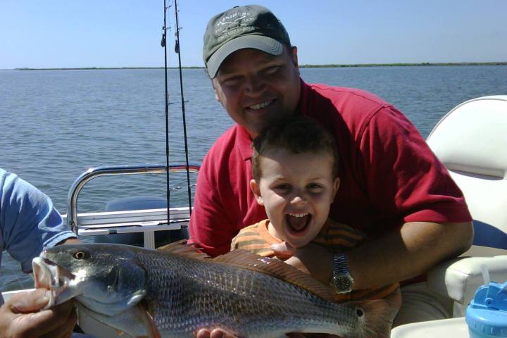 a man and a child holding a caught fish on a boat in a body of water